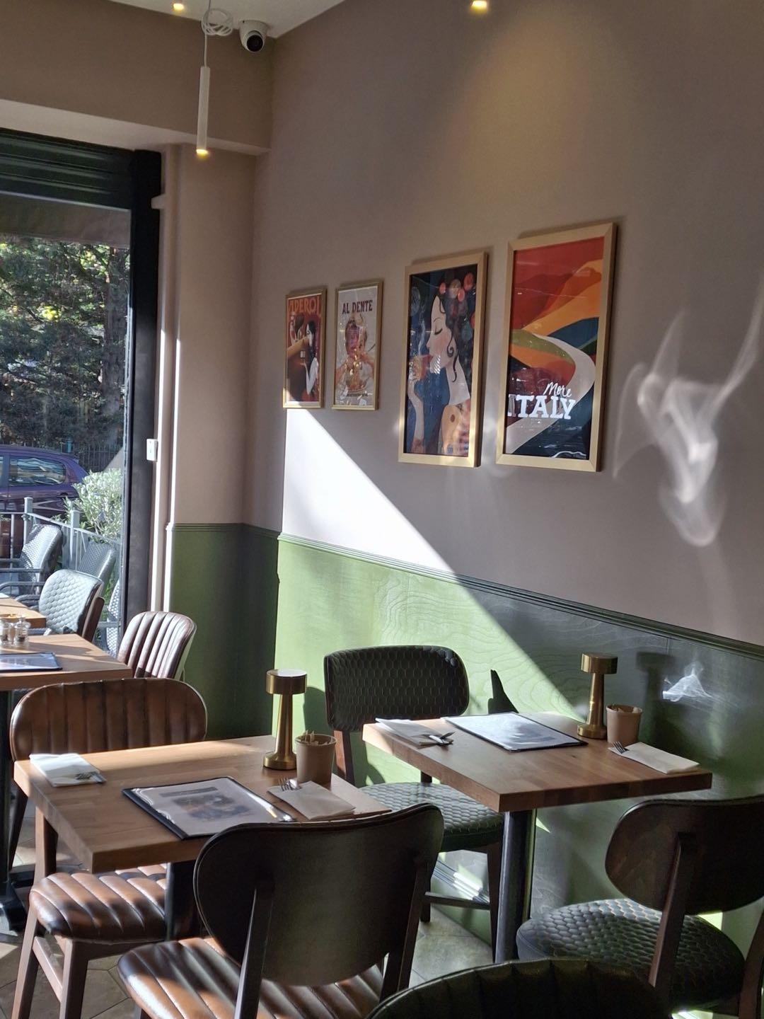 Inside Zefiro: sage-green panelled walls, warm oak tables, leather chairs and framed Italian posters, with the window onto Wanstead High Street
